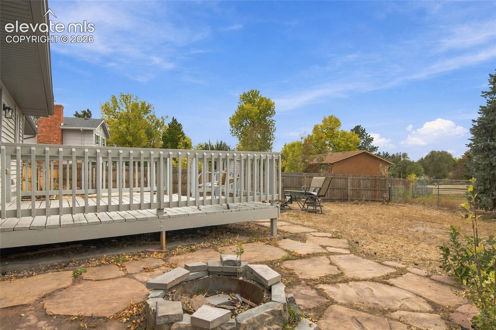 Raised wood deck with integrated railing, stone-paved patio, and a stone-lined fire pit
