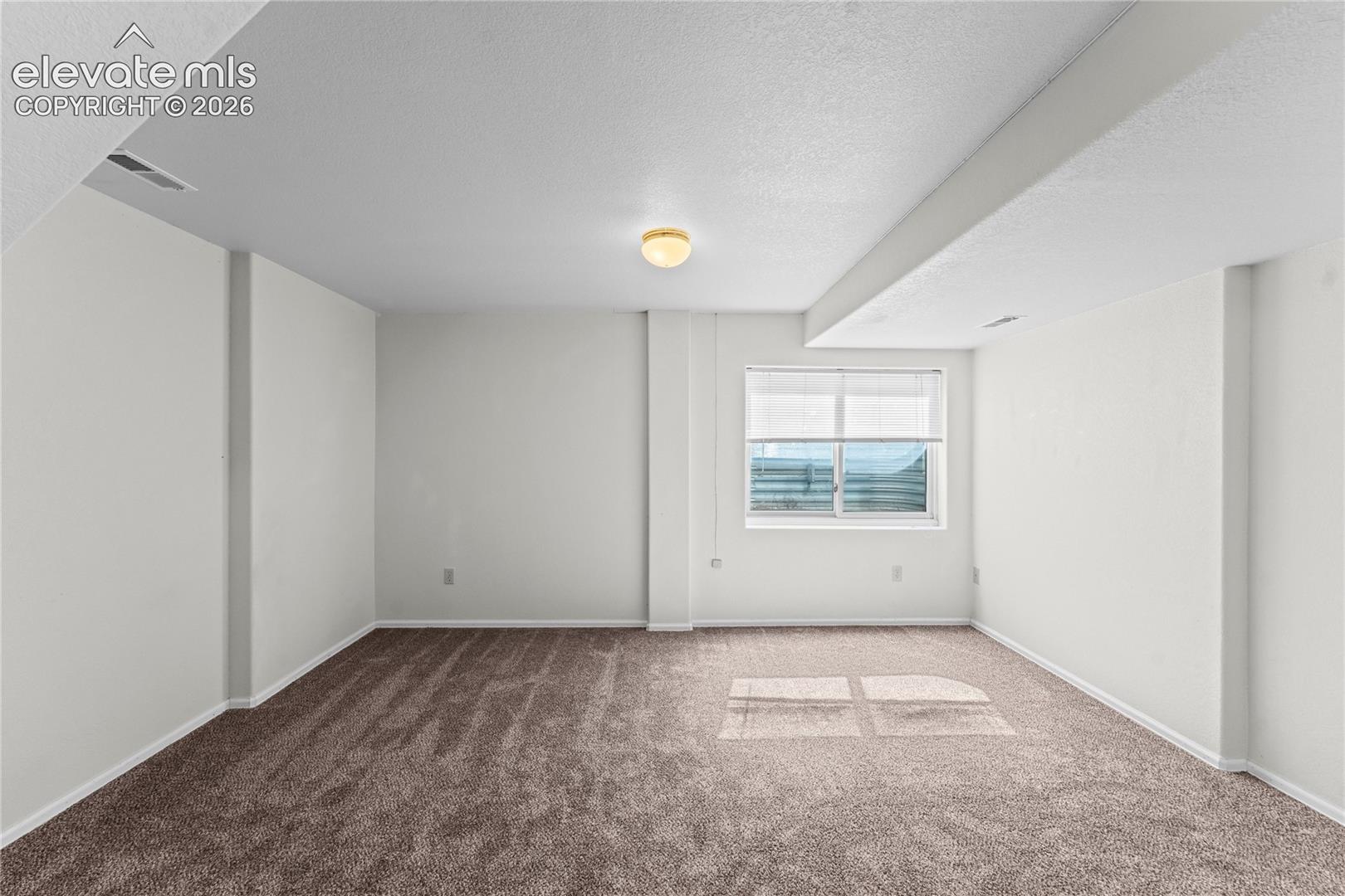 Recessed window with blinds, overhead lighting, textured ceiling, and neutral-toned carpeting