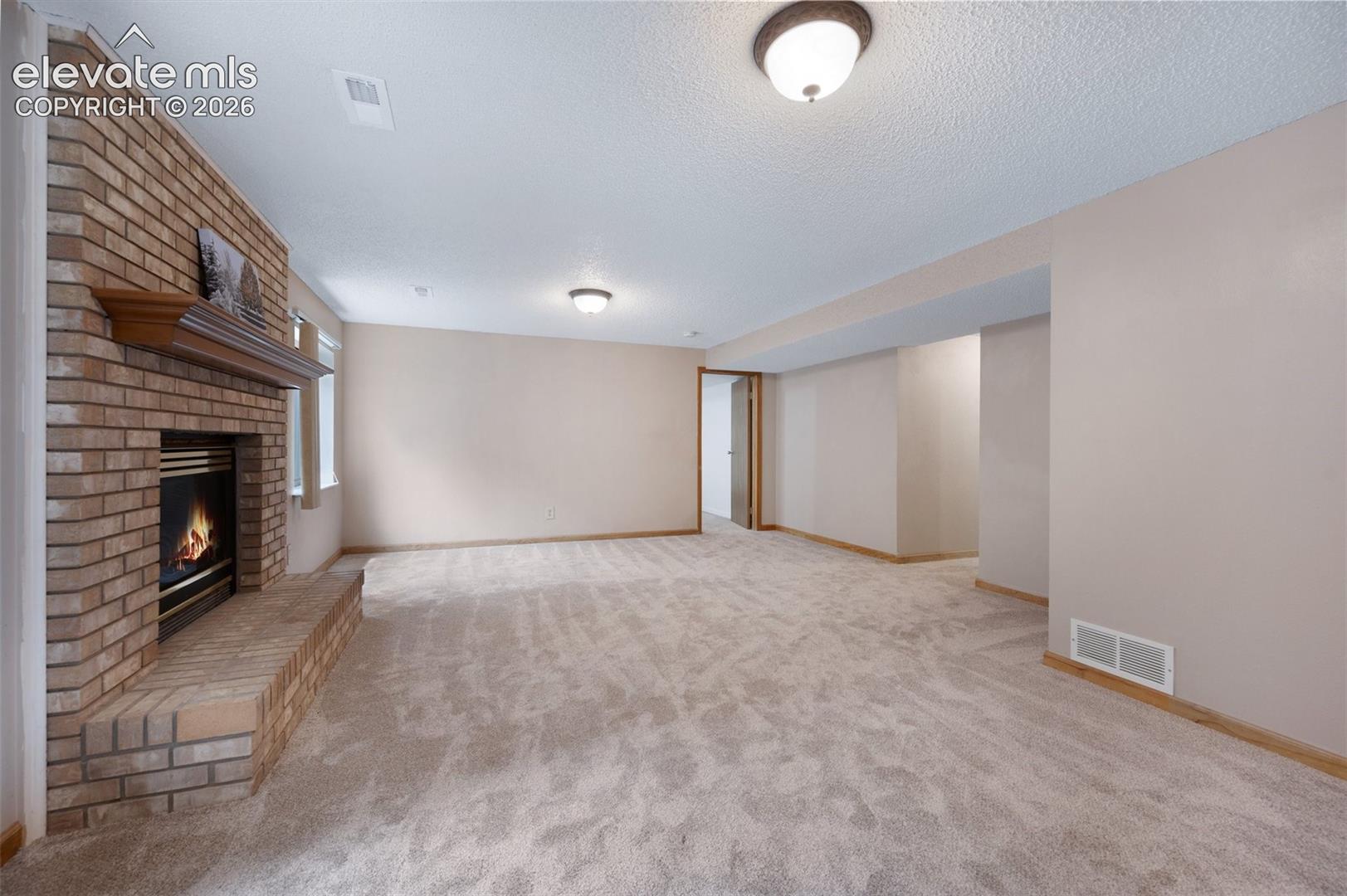 Unfurnished living room featuring carpet, a brick fireplace, baseboards, and a textured ceiling. fireplace staged and added.