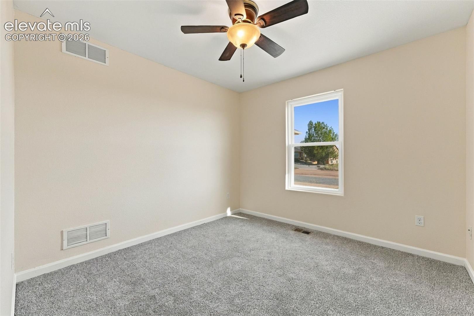 Neutral wall color, grey carpeting, and a ceiling-mounted light fixture with a fan