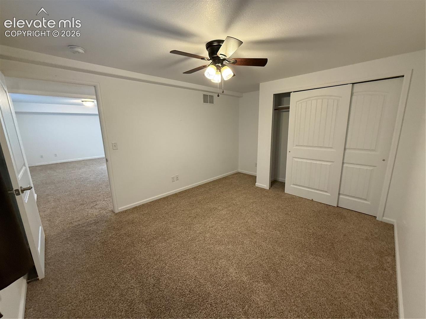 Neutral-toned carpeting, ceiling fan with integrated lighting, and closet with white paneled sliding doors