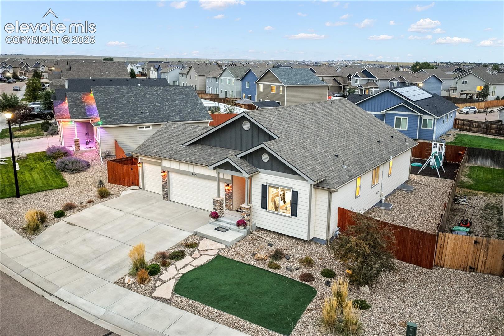 Two-car garage, stone accents, concrete driveway, front yard landscaping with artificial turf and decorative rock, and privacy fencing