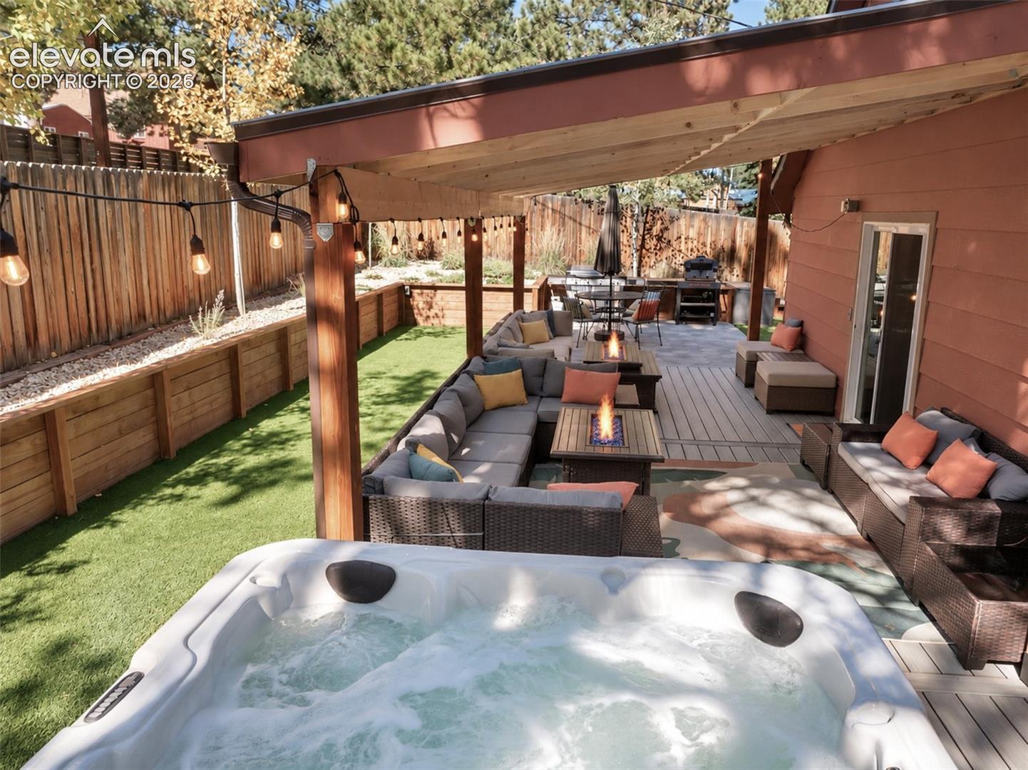 Covered outdoor patio with composite decking, fenced yard, synthetic turf, and exterior hot tub