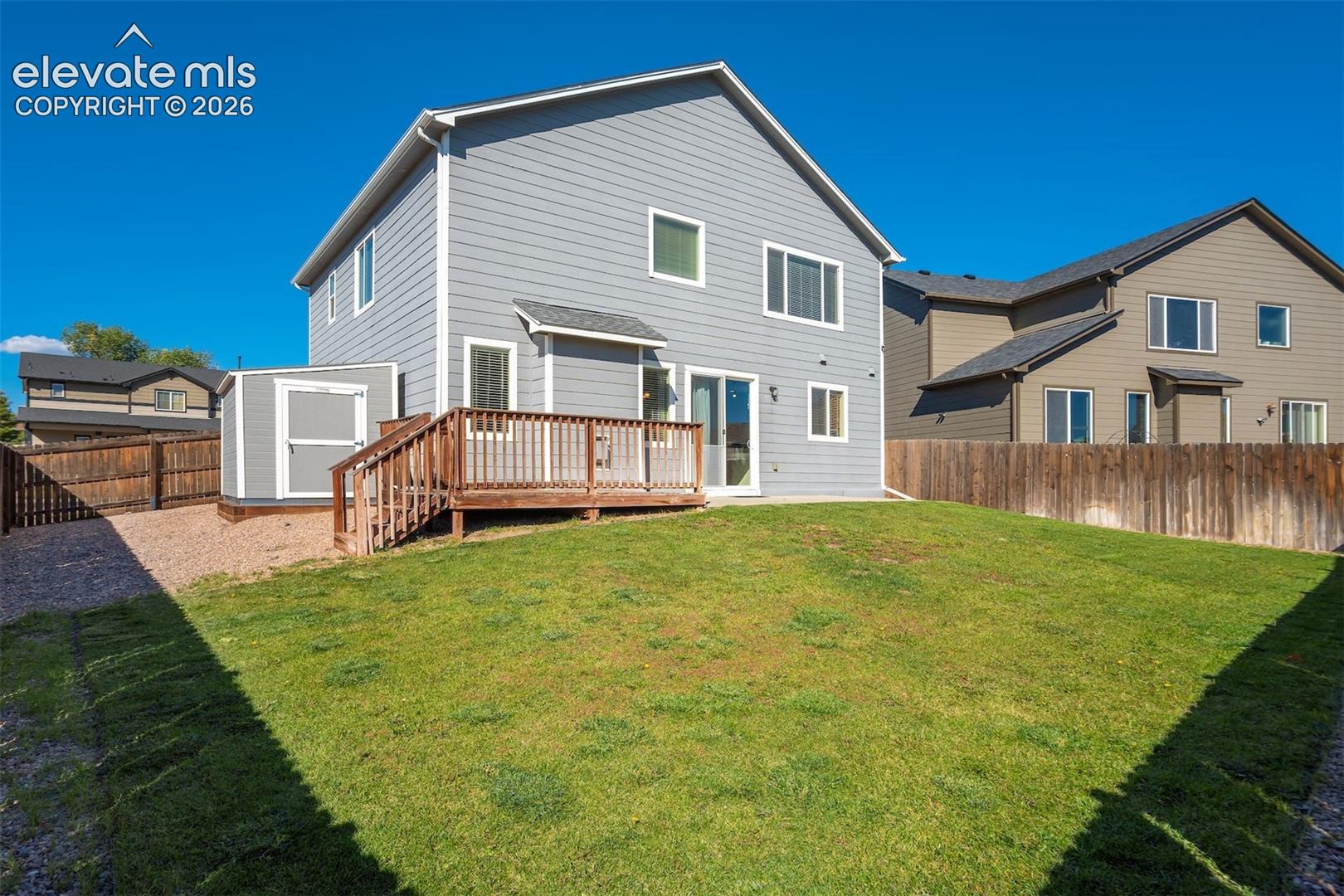 Expansive backyard with a manicured lawn, a wooden deck with railing, and a storage shed