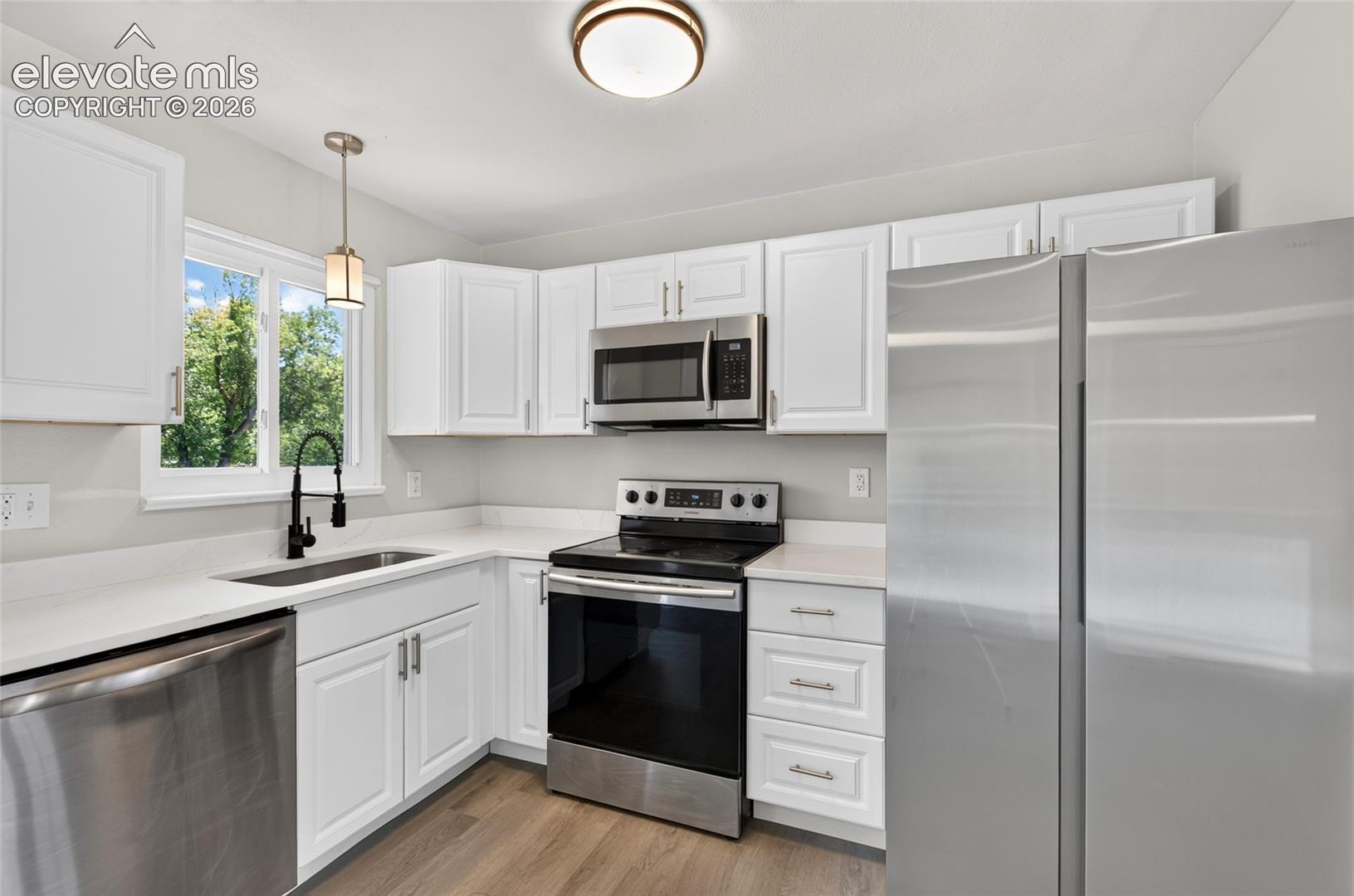 Modern kitchen featuring white cabinetry, stainless steel appliances, light countertops, and wood-finish flooring