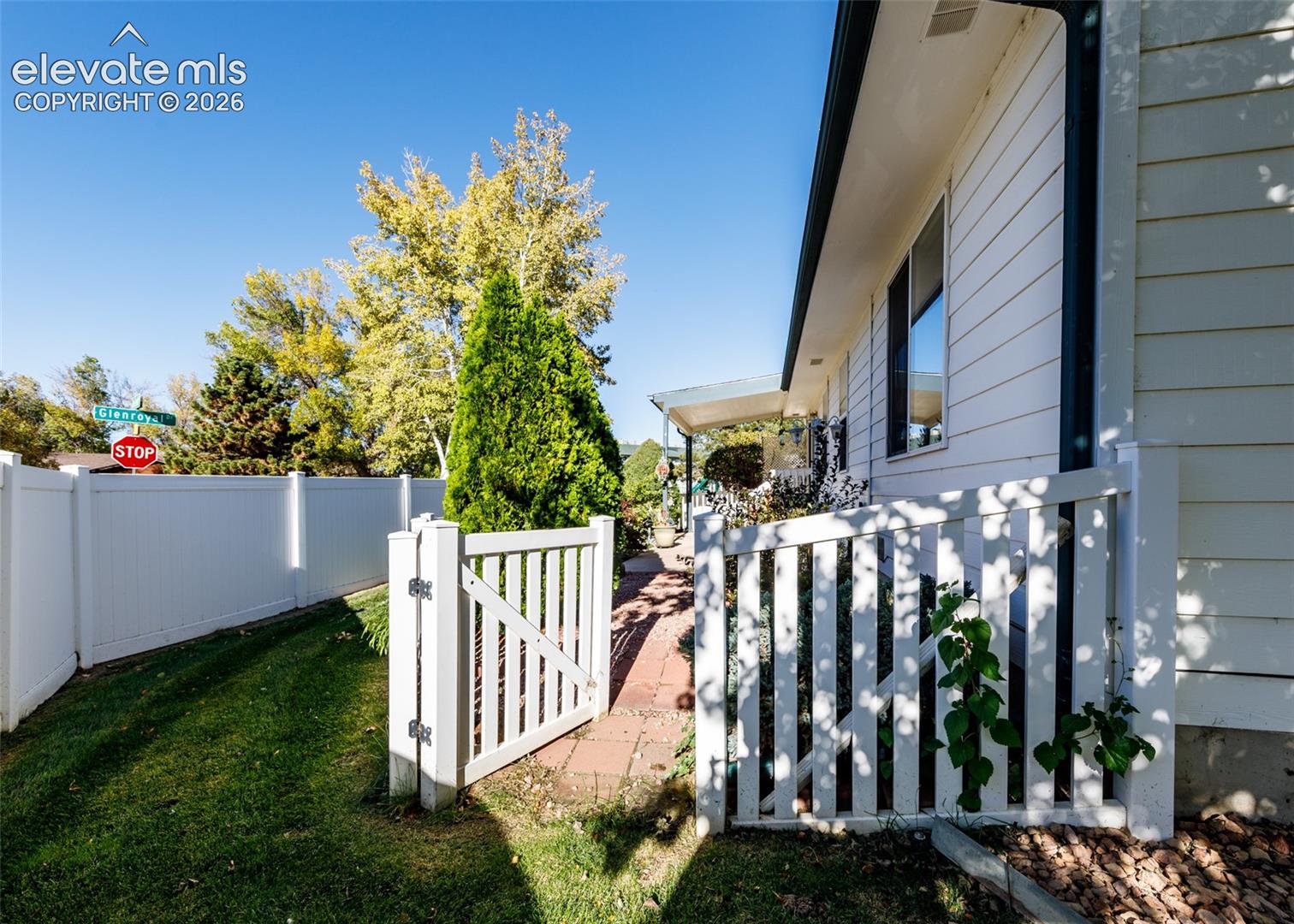 Exterior side yard featuring horizontal siding, a red brick pathway, a white vinyl perimeter fence, and a gated white picket fence