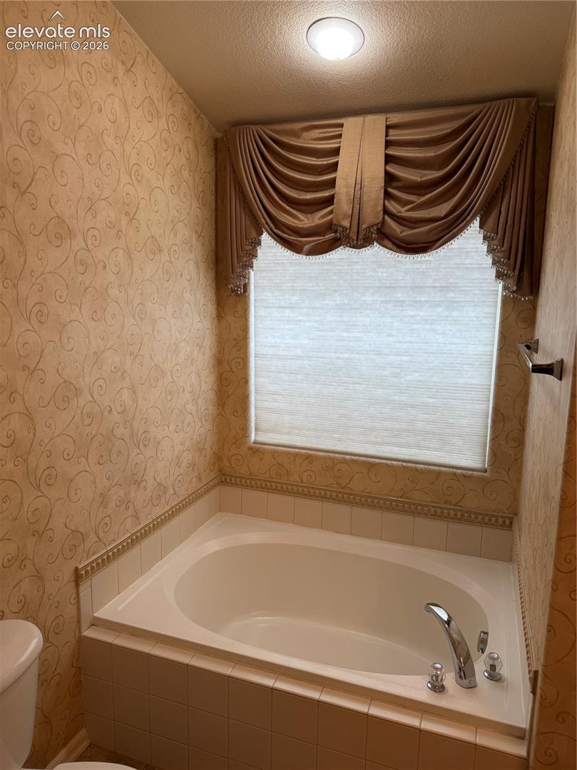 Built-in soaking tub with a tiled surround, patterned wall covering, and chrome faucet hardware