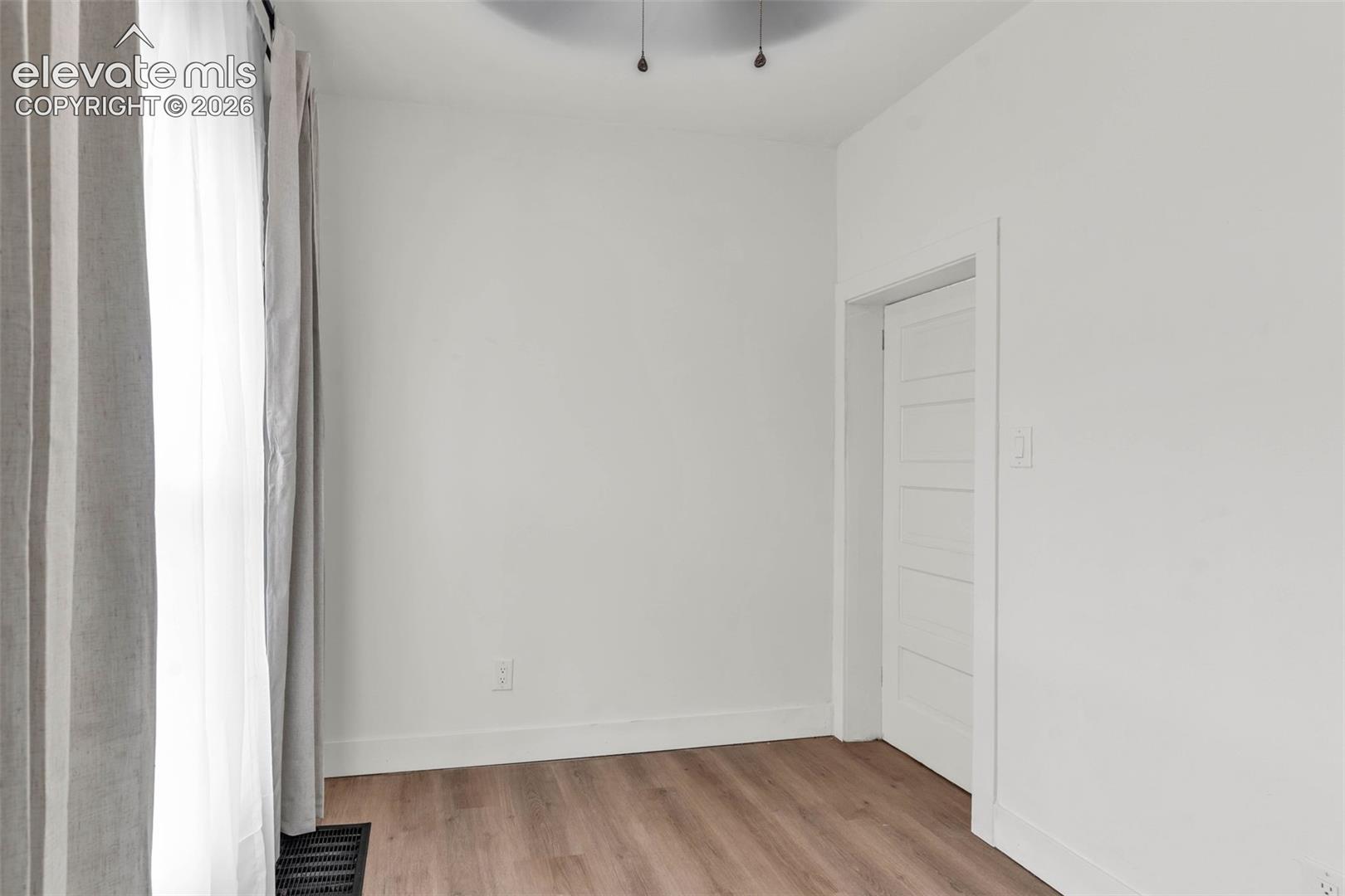 Room featuring wood-finish flooring, a white five-panel interior door, and a ceiling-mounted light fixture
