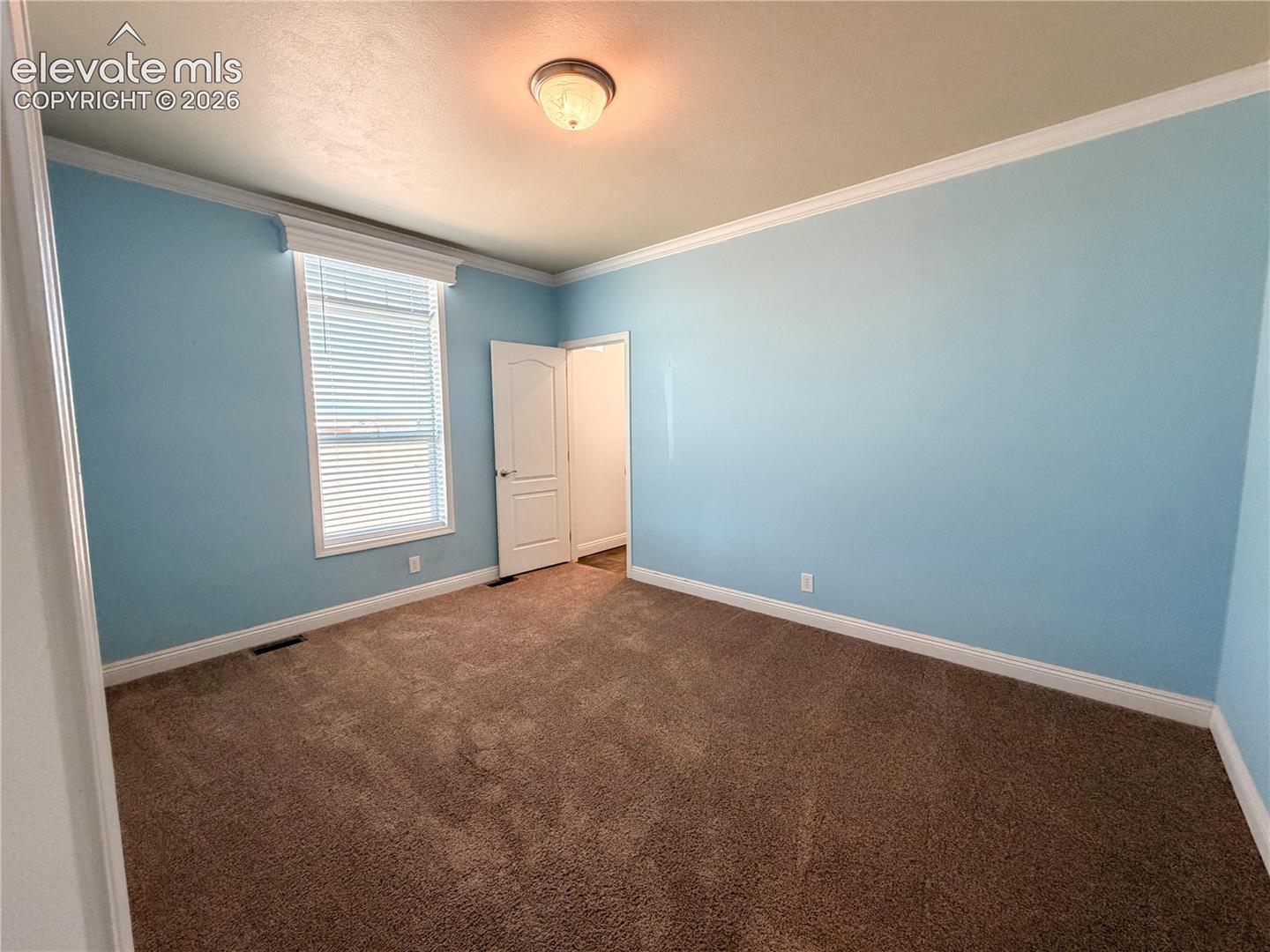 Room with neutral carpeting, crown molding, a window with horizontal blinds, and a multi-panel interior door