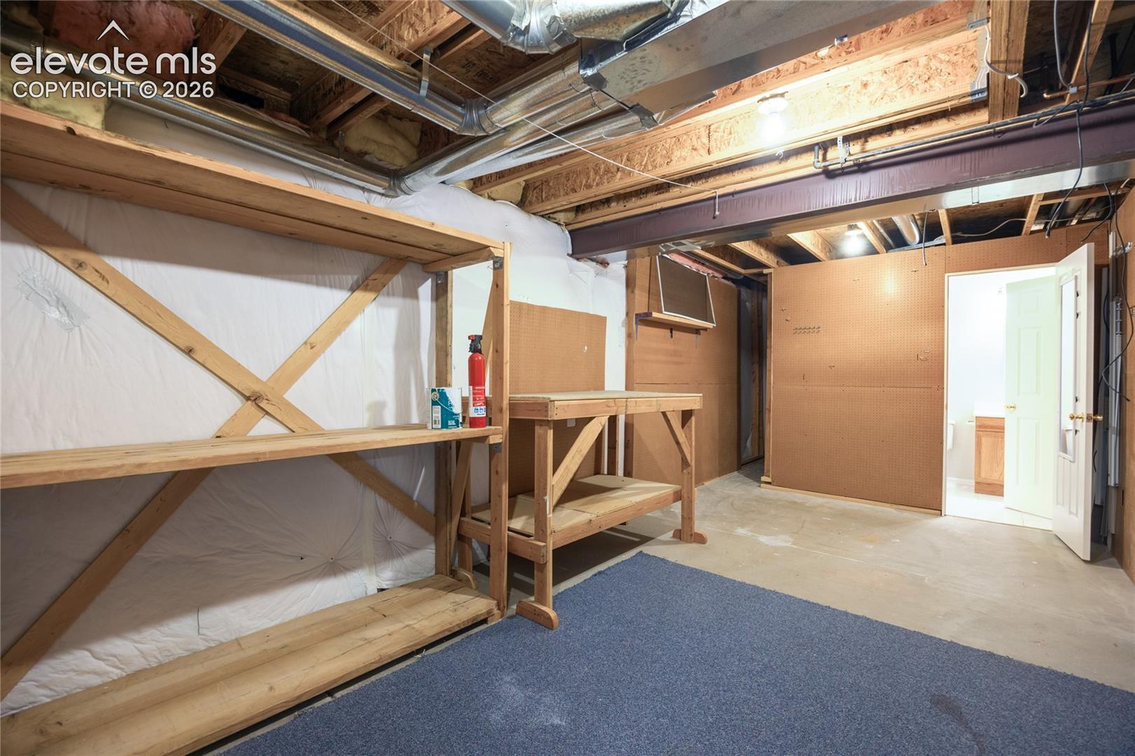 Unfinished basement storage area featuring wood-frame built-in shelving, exposed joist ceiling, concrete flooring, and solid core wood paneling