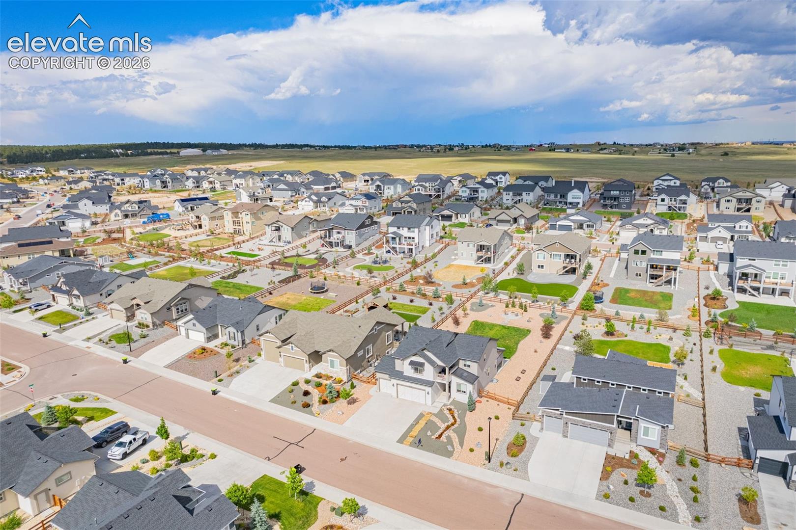 Aerial perspective of a suburban neighborhood featuring paved streets, detached single-family residences, landscaped front yards, concrete driveways, and expansive surrounding open space