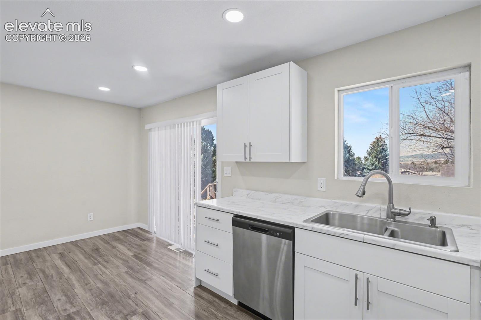 Kitchen featuring white cabinetry, stone-finish countertops, stainless steel dual-basin sink with high-arc faucet, stainless steel dishwasher, and wood-finish flooring