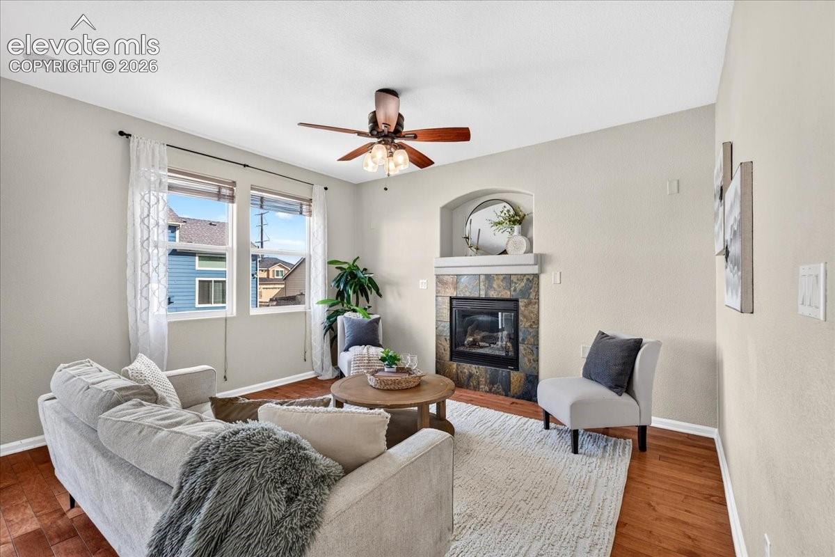 Living space featuring wood-finish flooring, a ceiling fan, and a fireplace with a stone surround