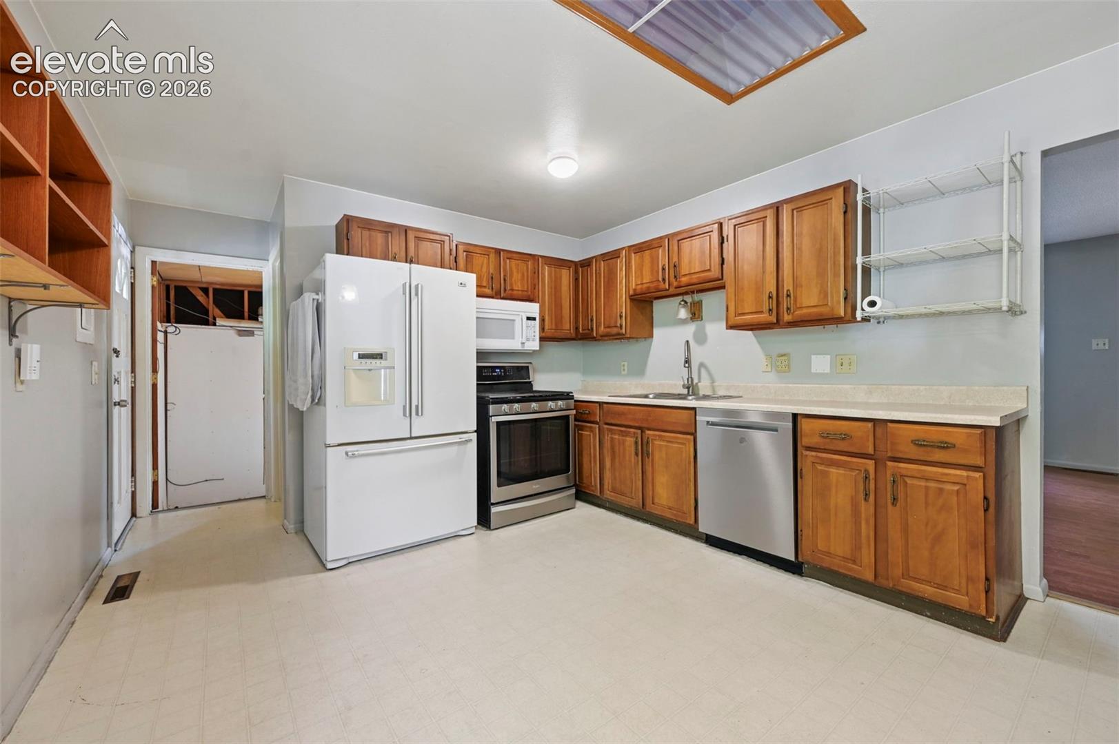 Kitchen featuring wood cabinetry, stainless steel appliances, a white refrigerator, a skylight, and light-toned flooring