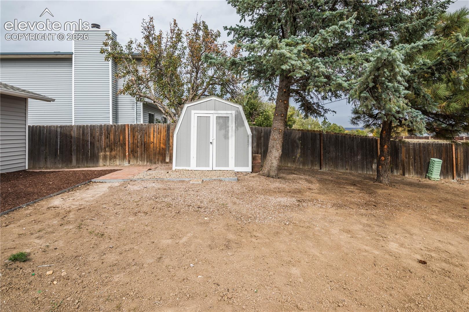 Rear yard featuring a detached storage shed, wood perimeter fencing, and mature evergreen trees