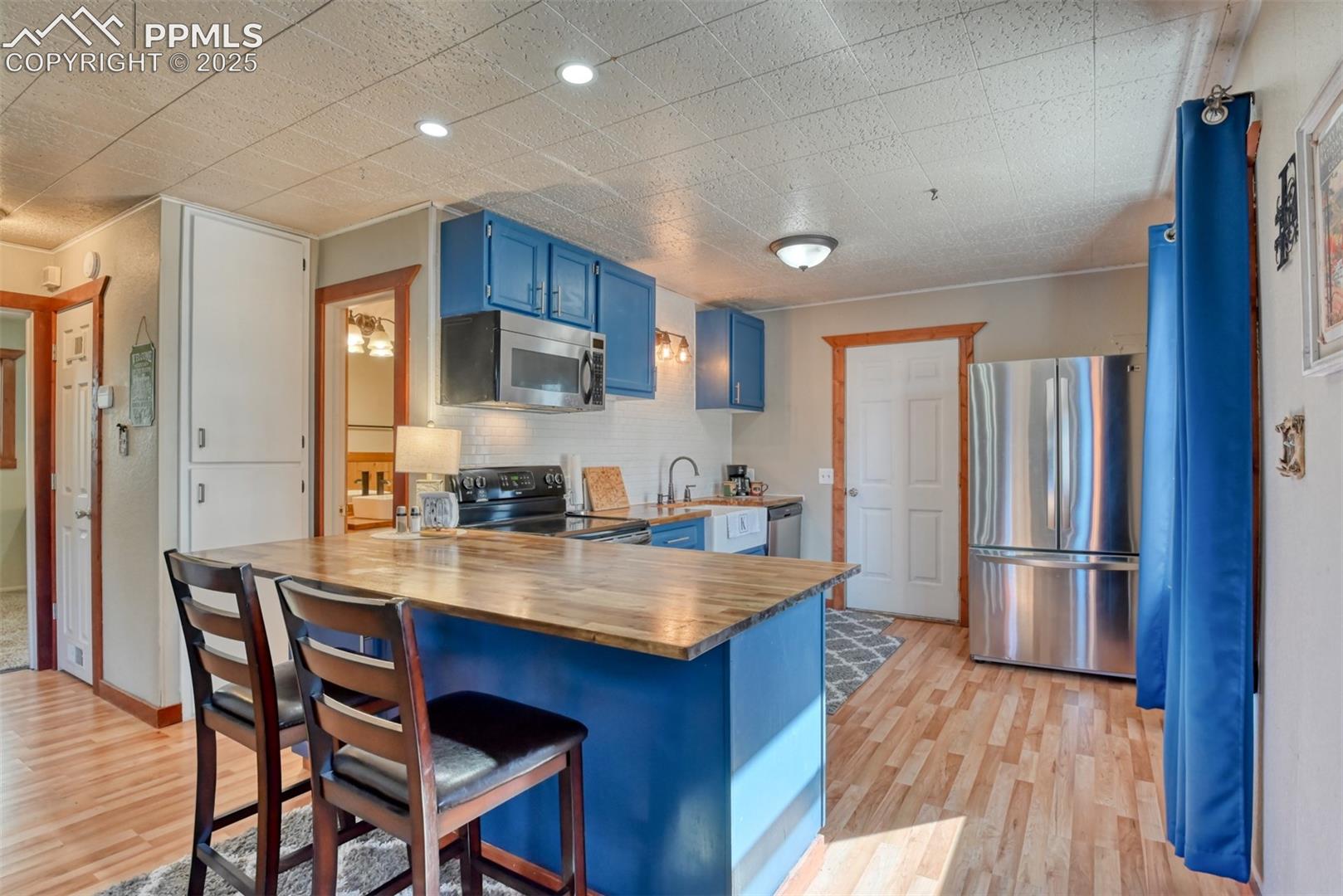 Kitchen with blue cabinets, butcher block countertops, a peninsula, appliances with stainless steel finishes, and a kitchen breakfast bar