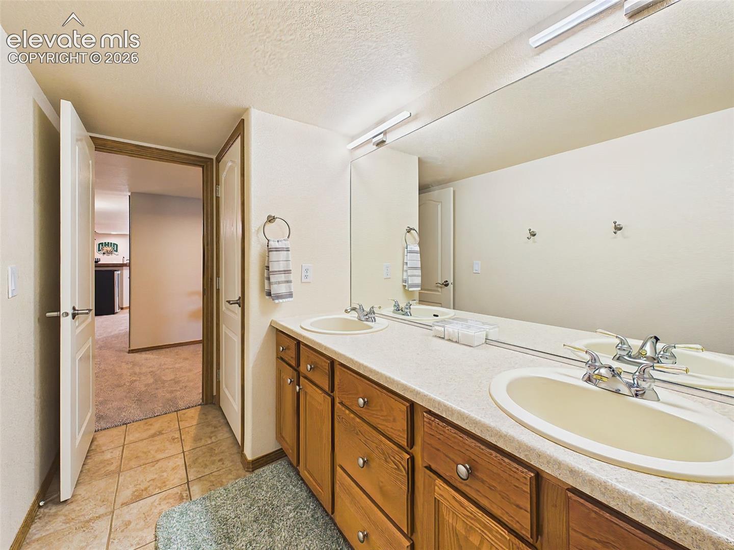 Well-appointed full bathroom with dual-sink vanity, abundant cabinet storage, and durable tile flooring.