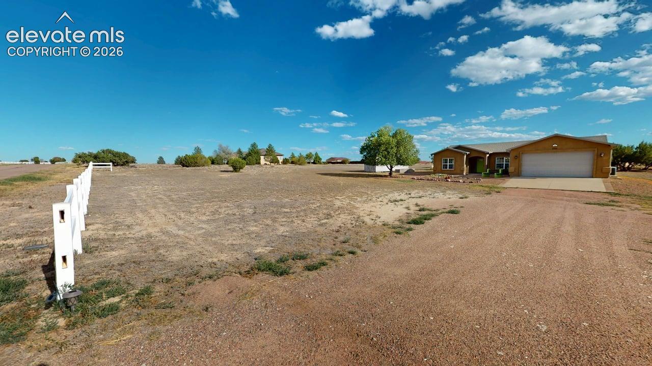 Ranch-style residence featuring an attached garage, white fencing, and a gravel driveway