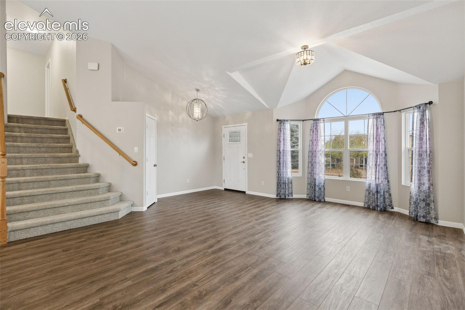 Vaulted ceilings, wood-finish flooring, staircase with a wood handrail, and an arched window