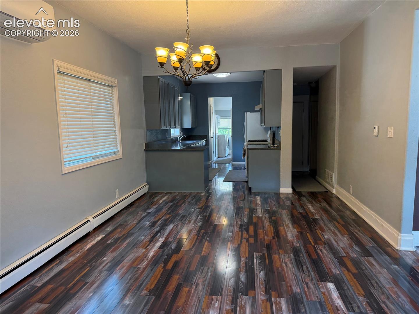 Multi-tonal wood-finish flooring, cabinetry with dark-toned surfaces, and a multi-light chandelier