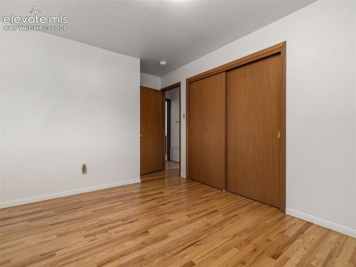 Hardwood flooring, white painted walls, wood-finish sliding closet doors, and a wood-finish interior door