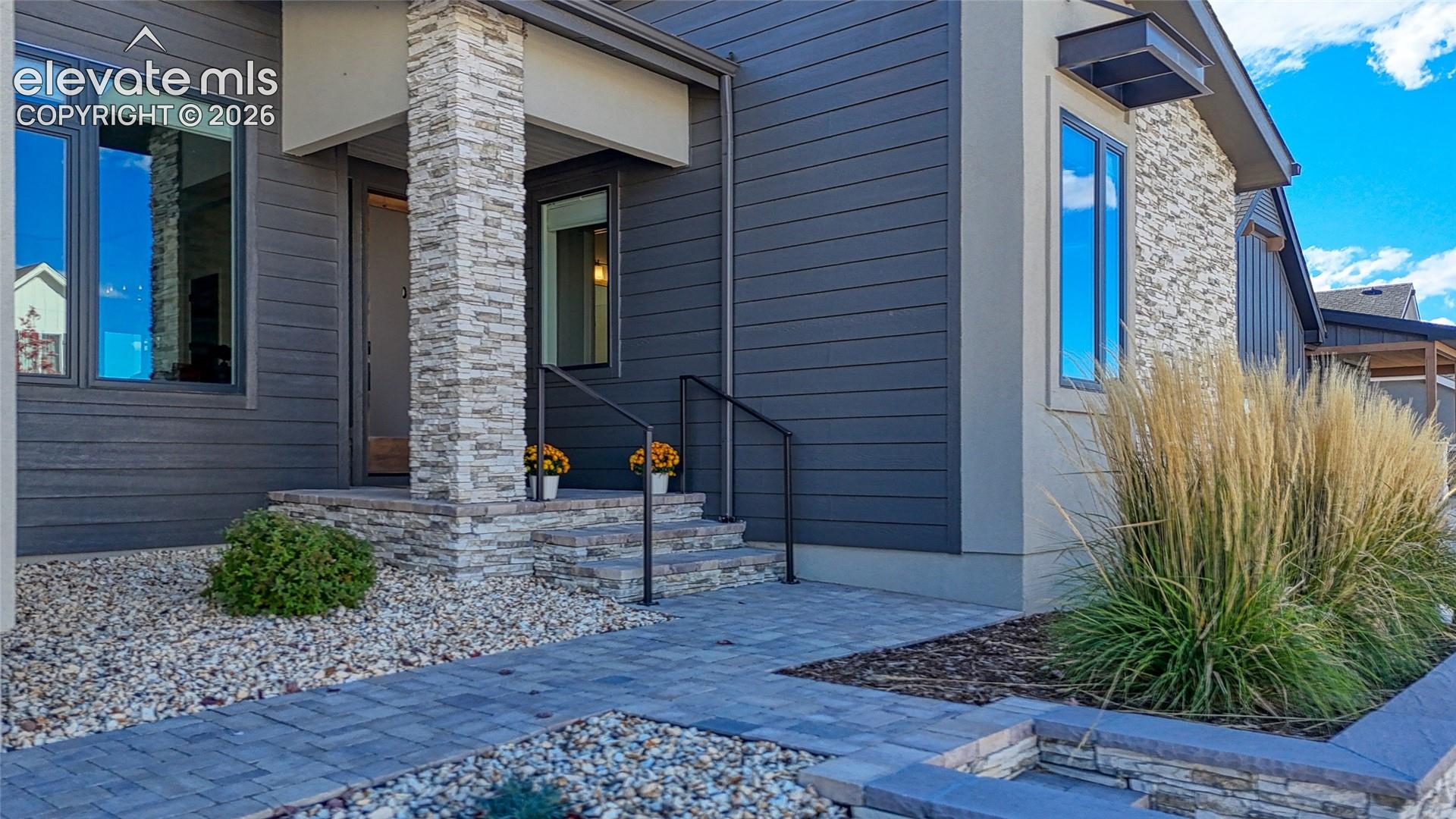 Exterior featuring dark horizontal siding, stacked stone accents, stone-clad entrance pillar, stone-paved walkway, and raised stone planter