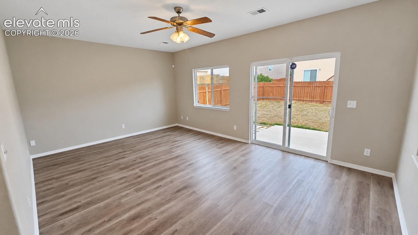 Room featuring wood-finish flooring, vaulted ceiling with a central fan, and sliding glass doors opening to a concrete patio and fenced backyard