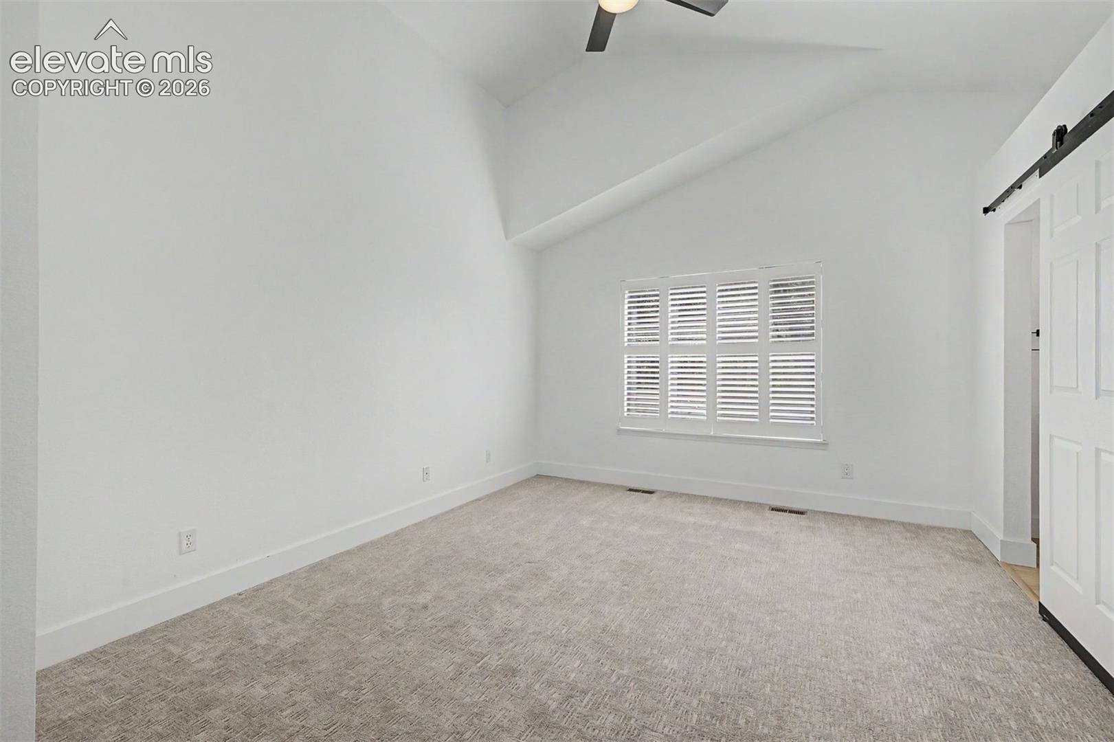 Primary bedroom with vaulted ceiling, ceiling fan, and ensuite bath