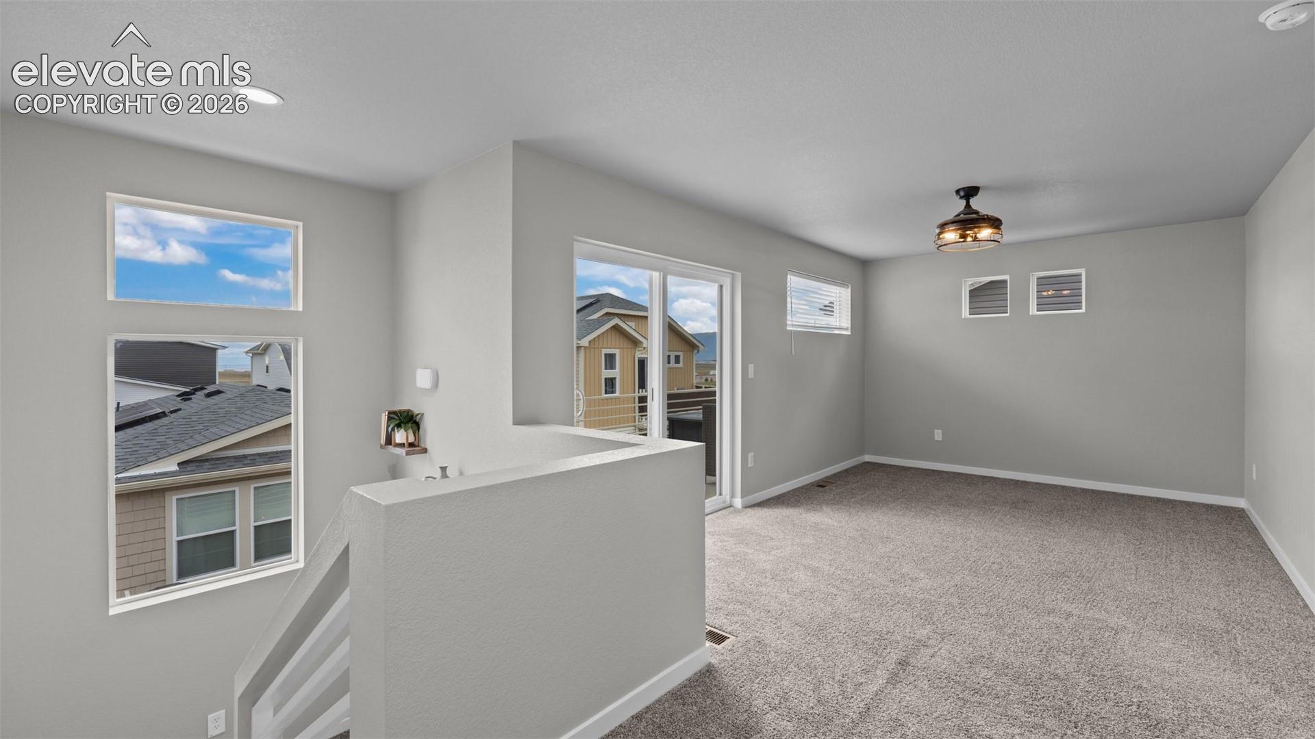 Open floor area featuring wall-to-wall carpeting, recessed ceiling lighting, a ceiling fan with integrated light fixture, multiple rectangular windows, and a sliding glass door