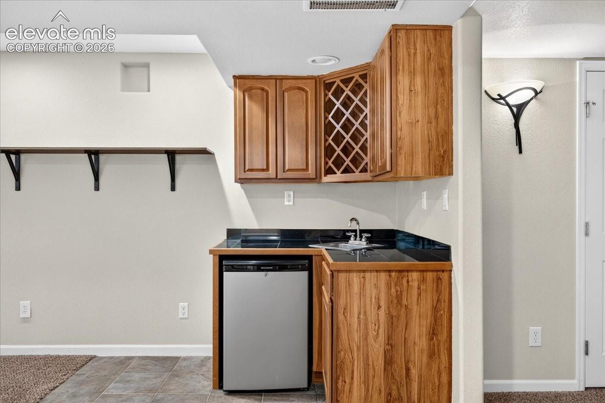 Compact wet bar featuring wood-finish cabinetry, integrated wine rack, and a stainless steel under-counter refrigerator