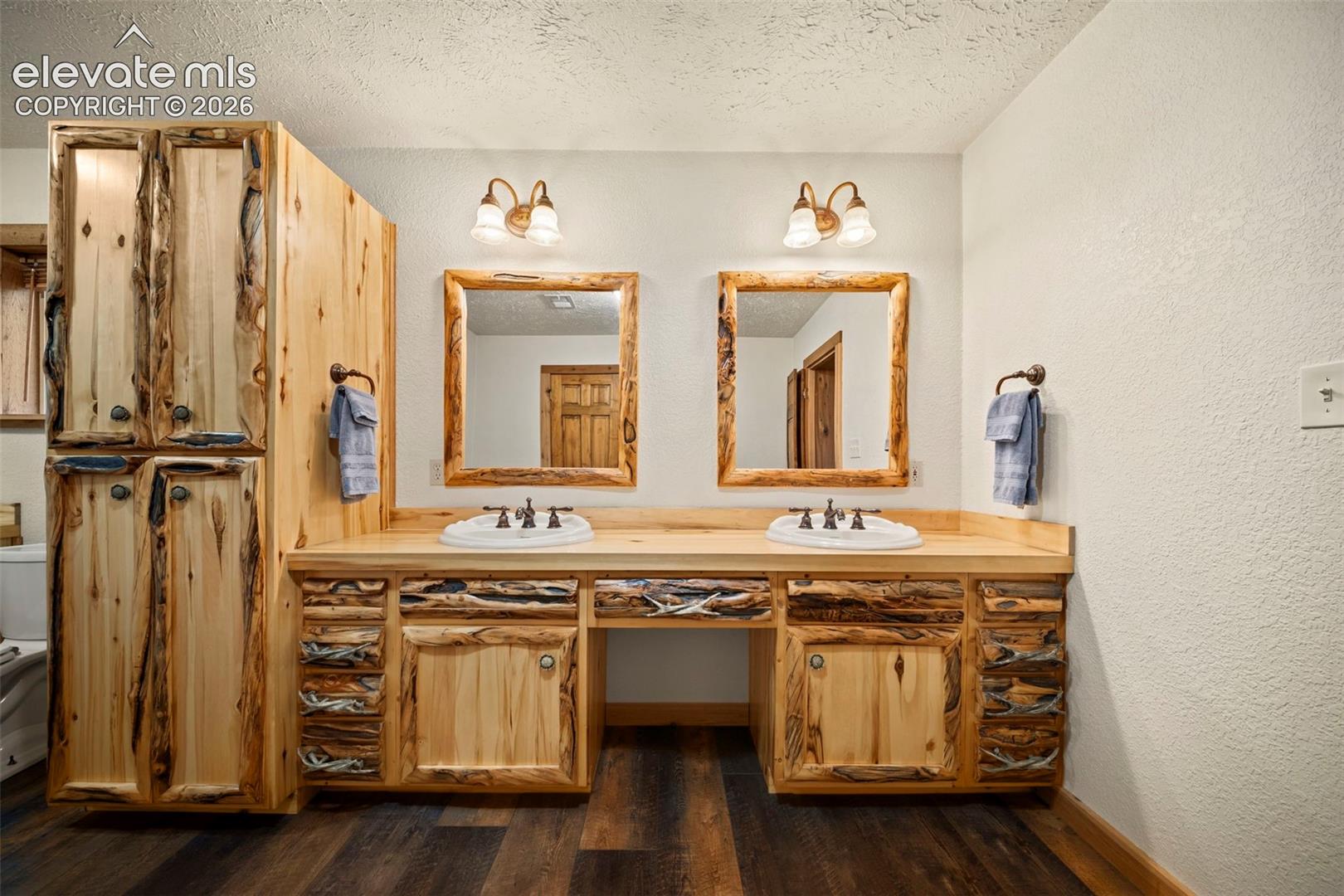 Custom natural-wood cabinetry featuring live-edge detailing, dual drop-in sinks, matching framed mirrors, and dual wall-mounted light fixtures