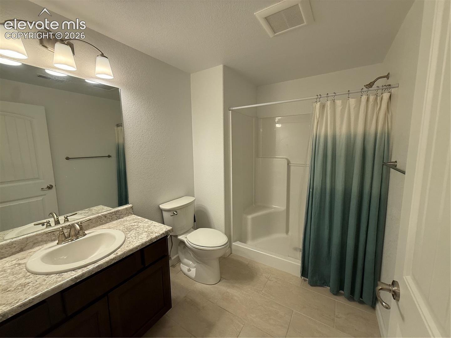 Bathroom featuring a vanity with a stone-finish countertop, undermount oval sink, three-light fixture, tile flooring, and a shower-tub combination with an integrated seat