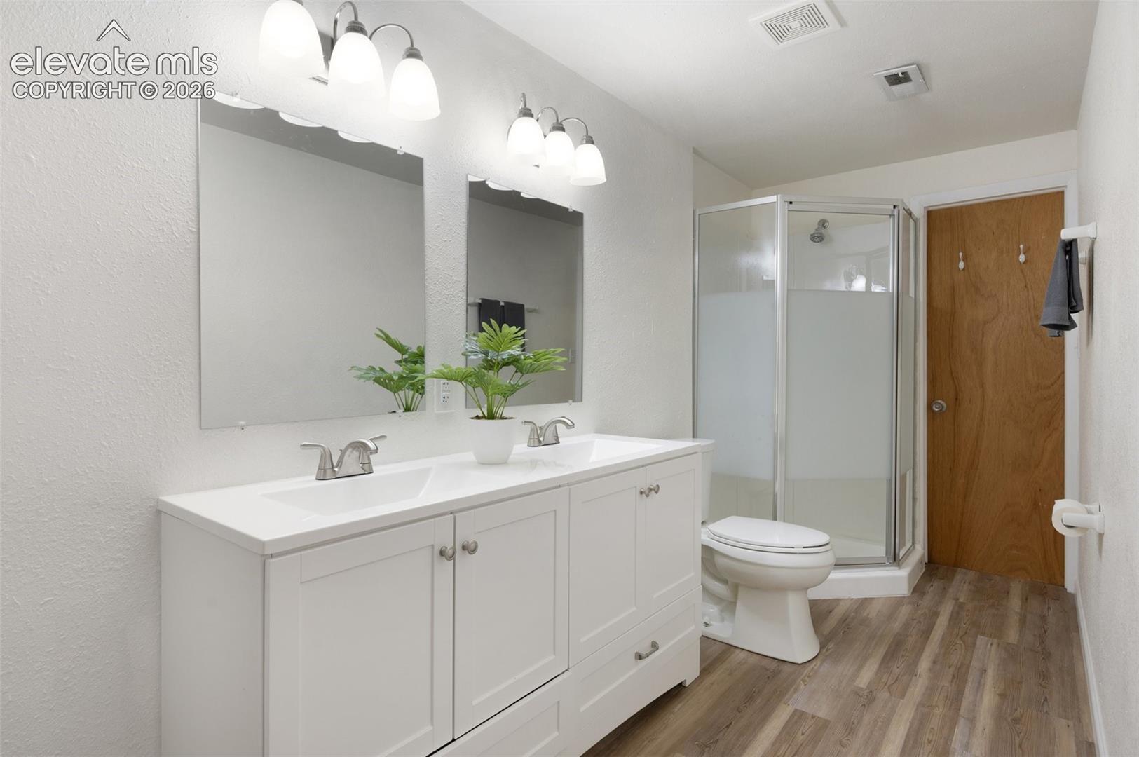 Full bath with wood finished floors, a stall shower, toilet, and double vanity