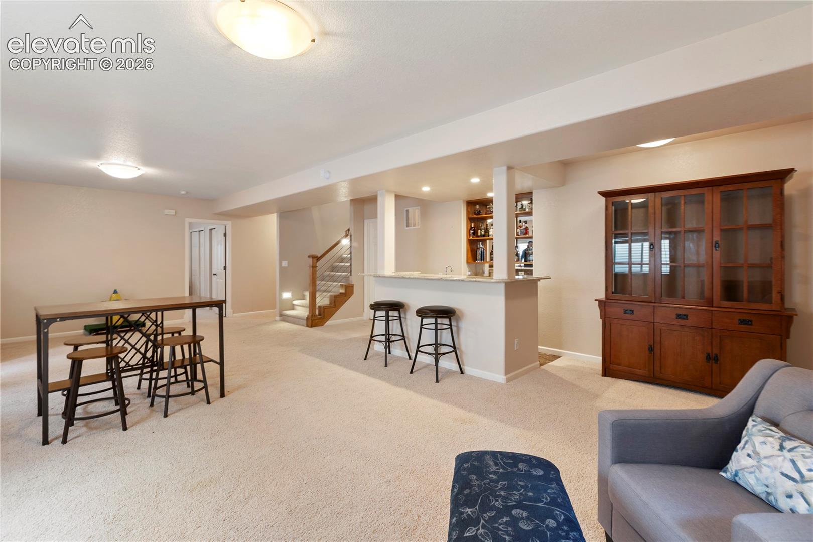 Expansive carpeted area featuring a built-in wet bar with shelving, a wooden staircase with metal railings, and dual closet doors