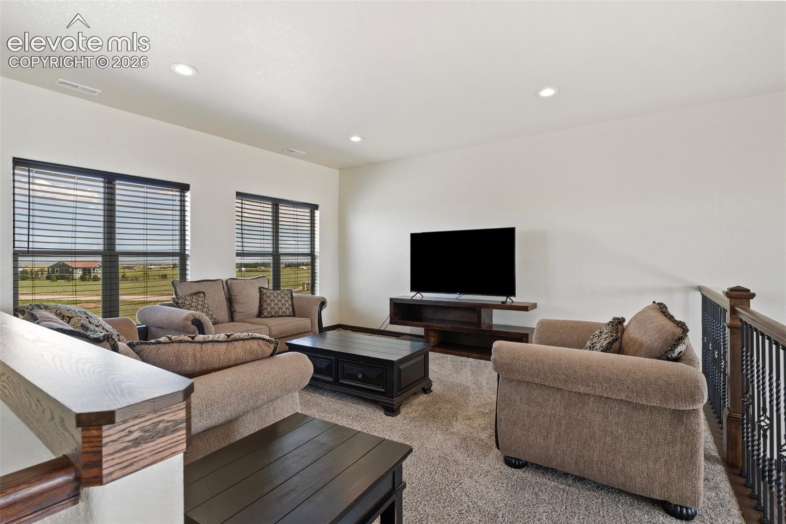 Open-concept loft/living area featuring two large windows with horizontal blinds and recessed ceiling lighting