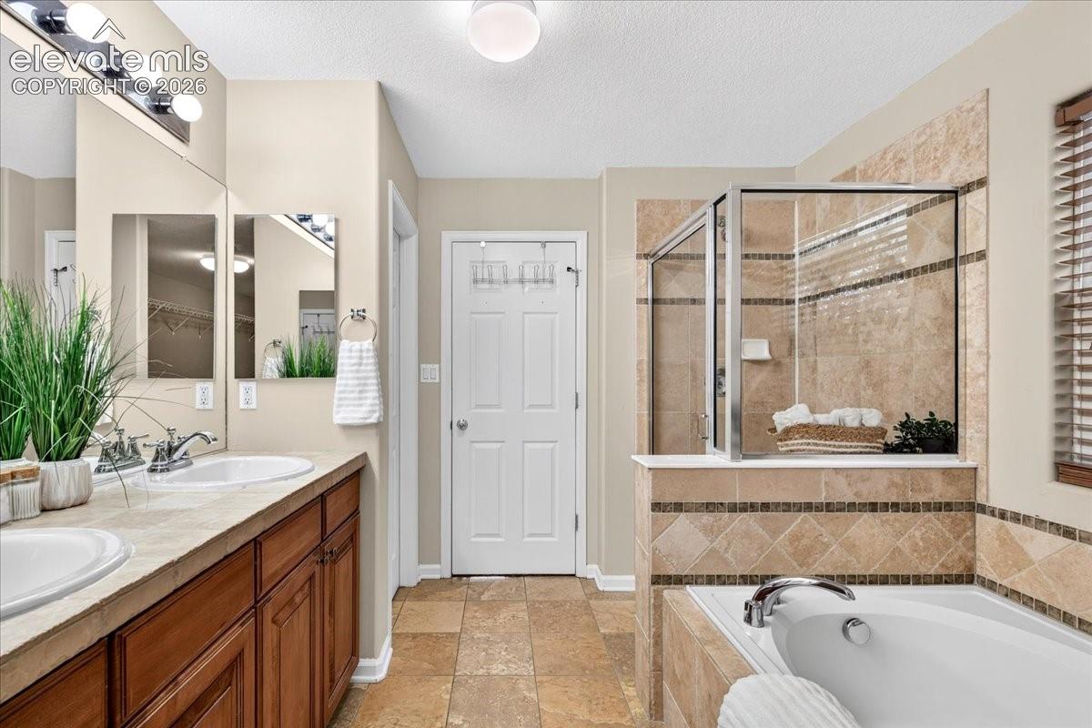 Dual vanity with under-sink storage, tile flooring, glass-enclosed shower, built-in bathtub, and tile accents