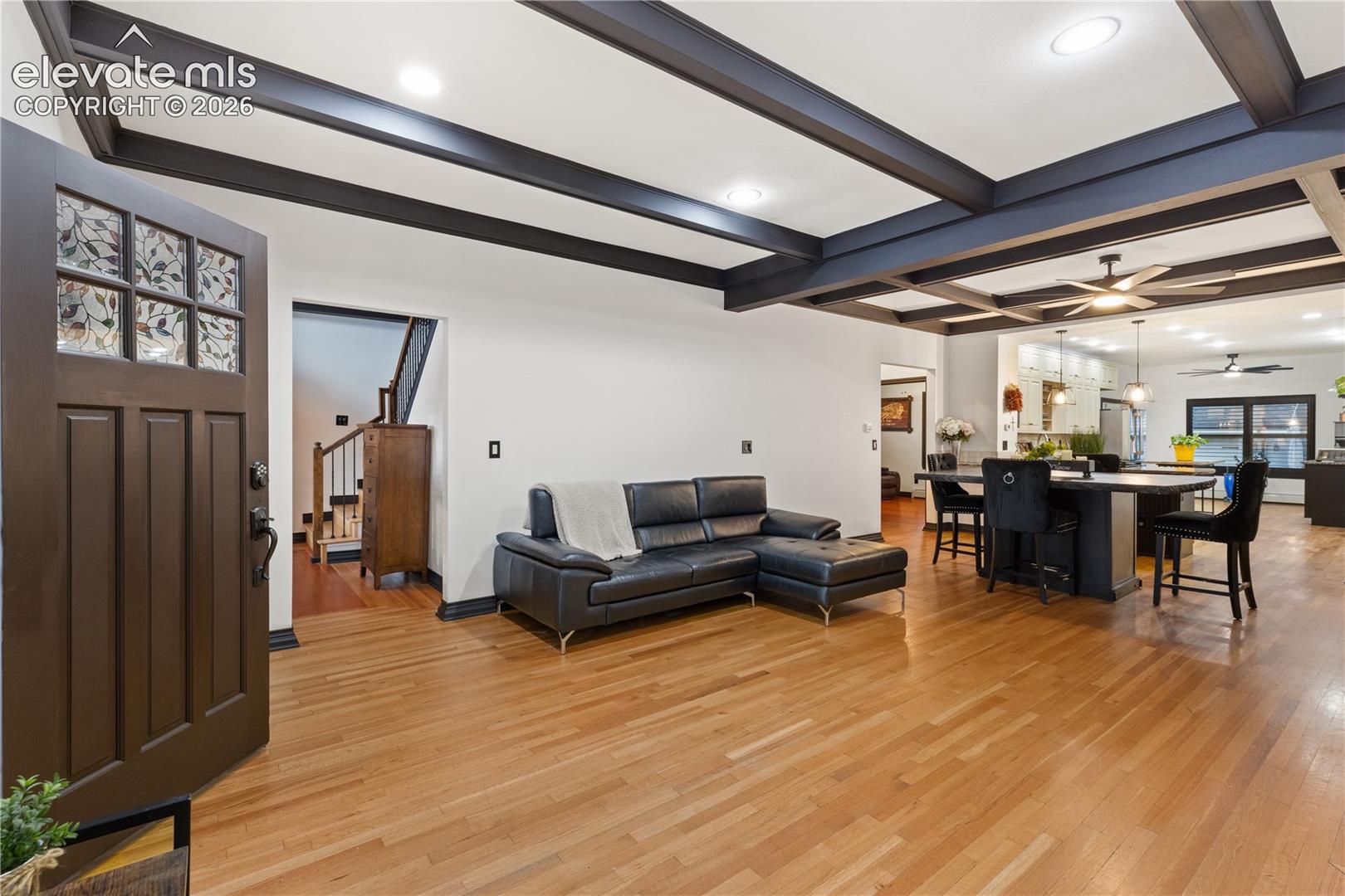 Solid wood entry door with decorative glass, hardwood flooring, coffered ceilings, recessed lighting, and a built-in island with seating