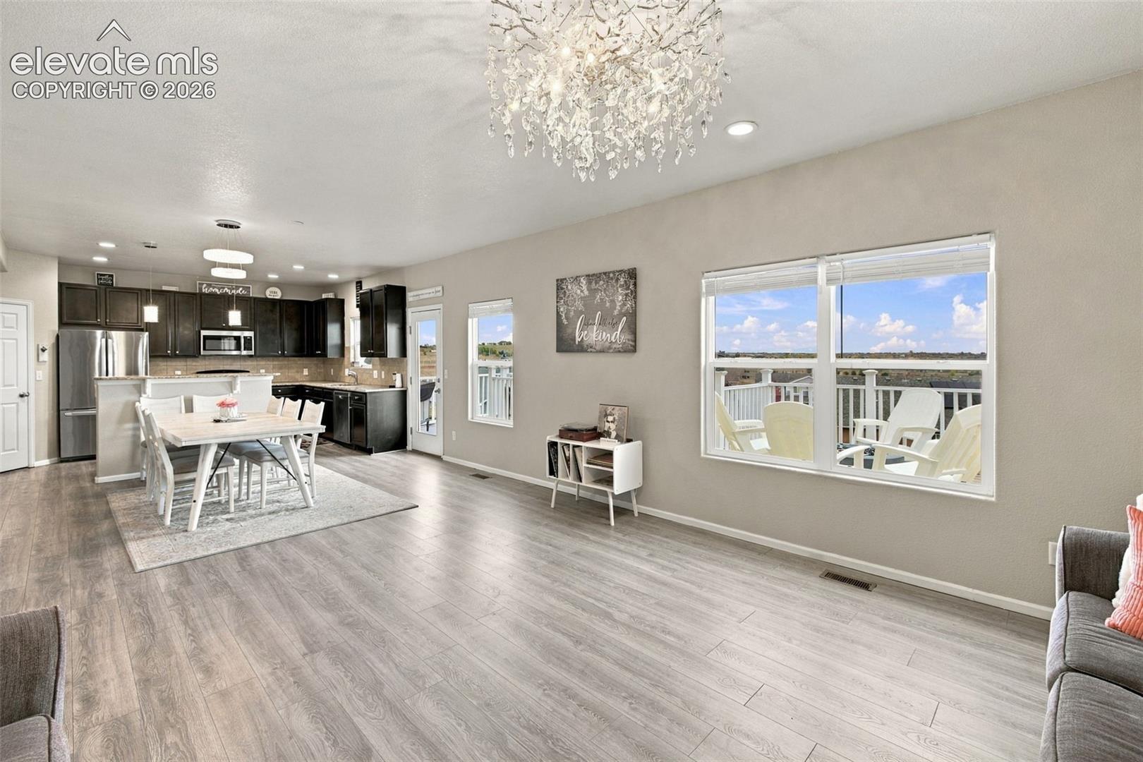 Open-concept kitchen and living area featuring wood-finish flooring, dark cabinetry, recessed lighting, and a decorative chandelier