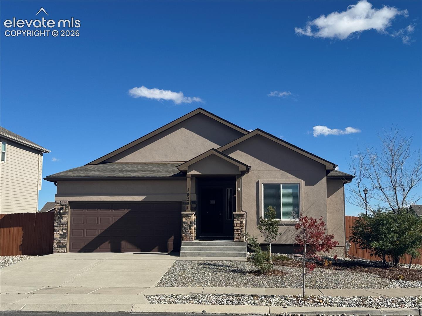 Stucco exterior featuring a dual-gable roofline, stone veneer accents, an attached two-car garage, and concrete driveway
