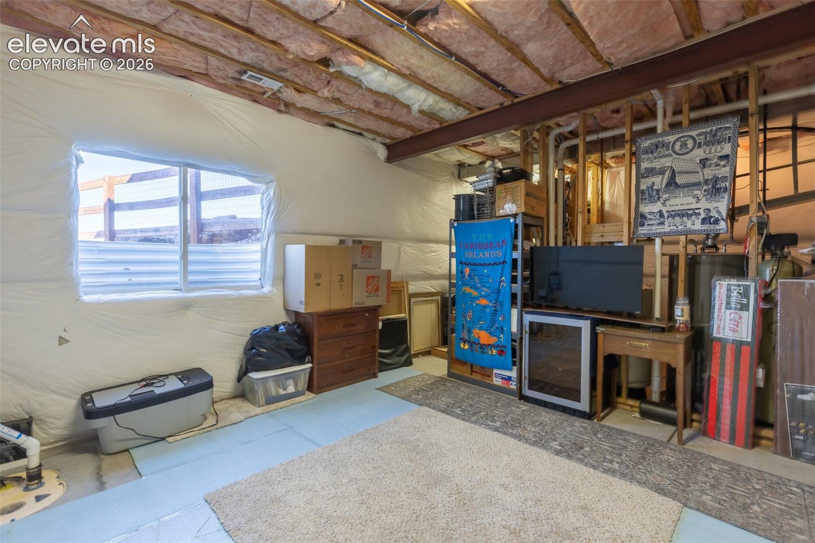 Unfinished lower level featuring exposed ceiling joists, concrete flooring, and an egress window with a corrugated metal window well