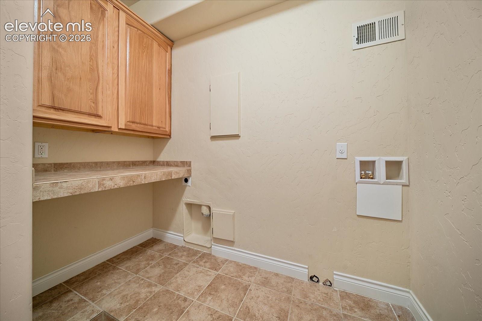 Laundry room featuring wood-finish cabinetry, tile-topped folding counter, and tiled flooring