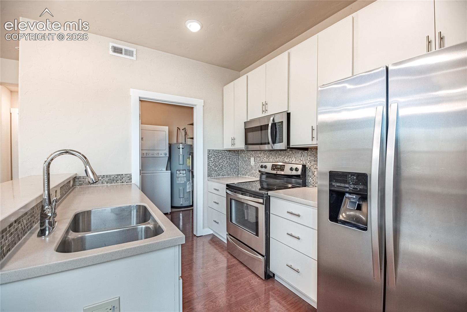 Kitchen featuring stainless steel appliances, white cabinetry, a double basin sink, light-toned countertops, and a patterned tile backsplash