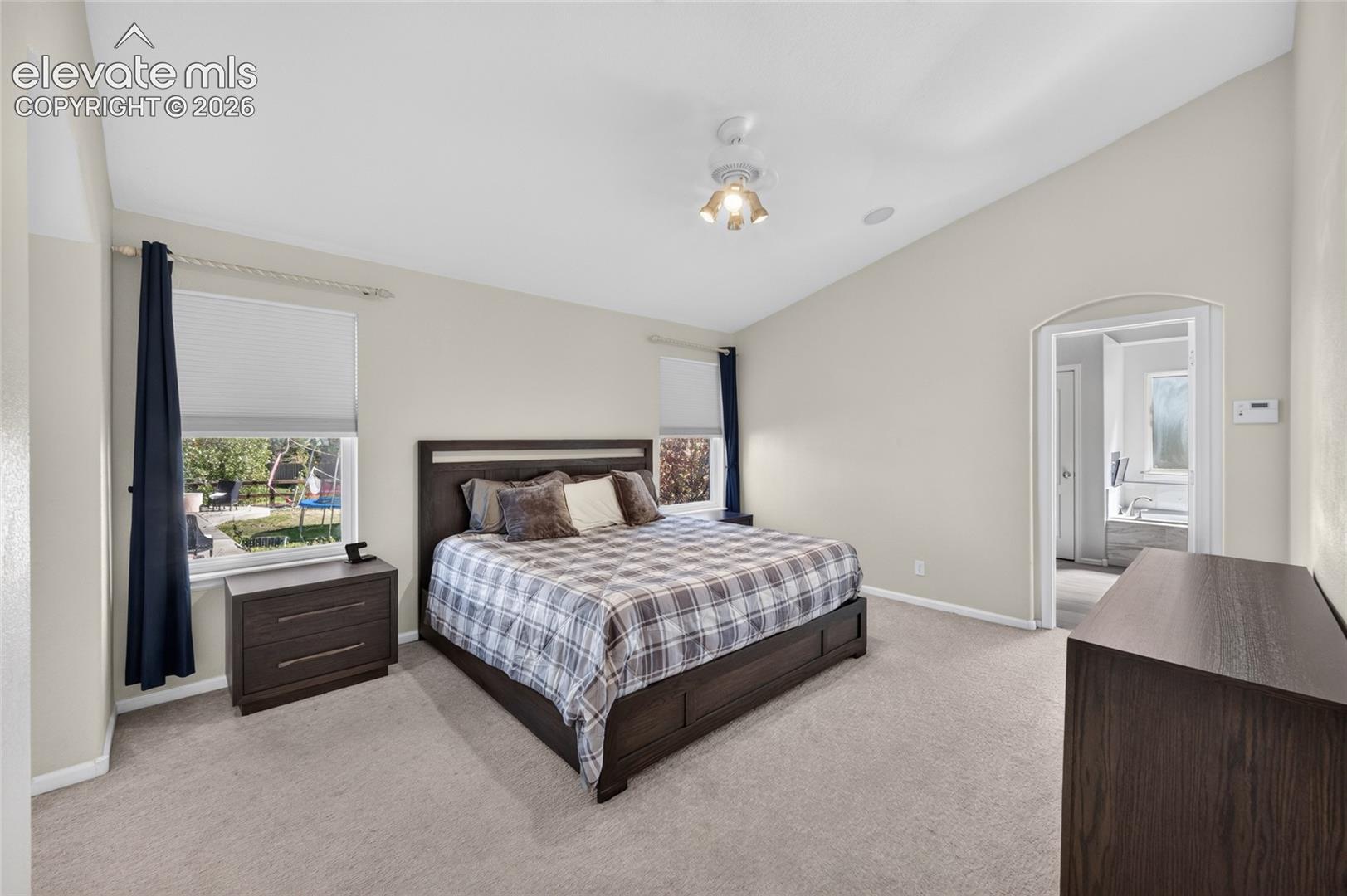 Vaulted ceilings, neutral wall tones, carpeted flooring, and a multi-light flush mount fixture