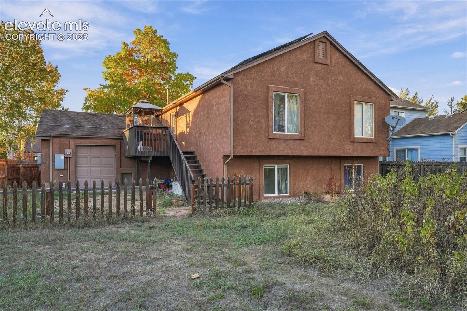 Exterior view featuring a textured stucco finish, elevated wooden deck with staircase, and an attached single-car garage