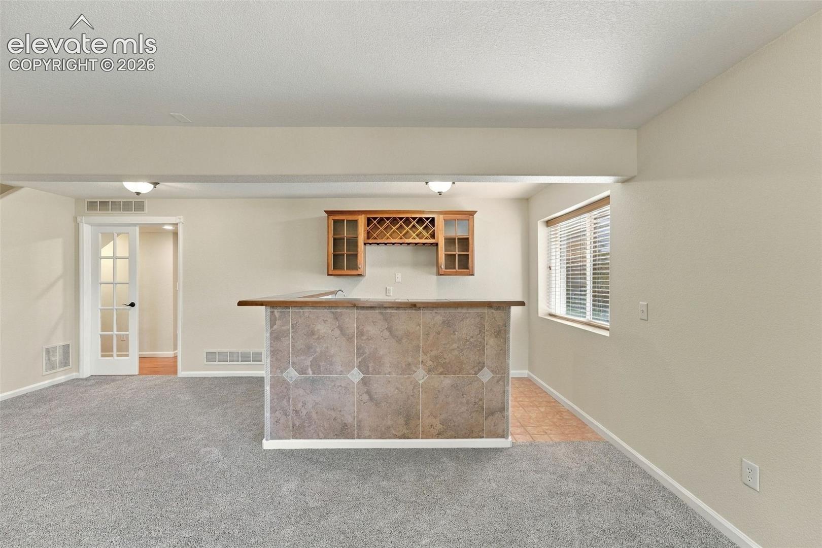 Built-in wet bar featuring stone tile facade, wood-finish countertop, and overhead cabinetry with integrated wine storage, accompanied by a French-style interior door and carpeted flooring