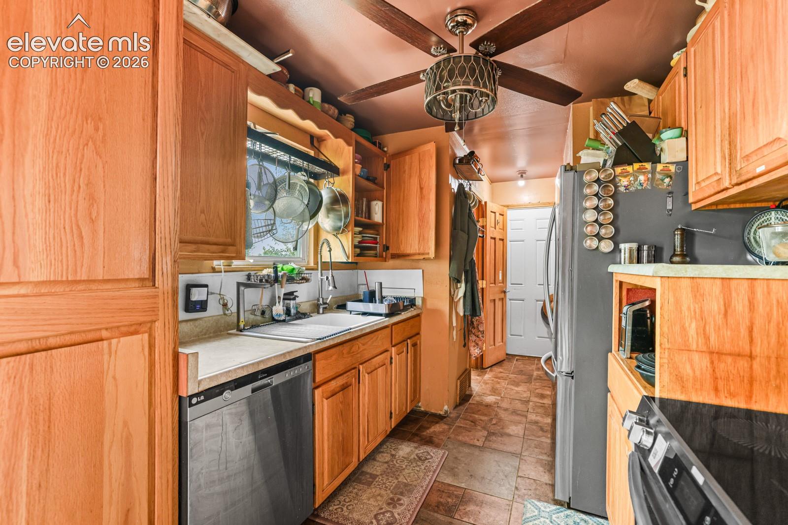 Kitchen featuring wood-finish cabinetry, solid surface countertops, a stainless steel dishwasher, and a ceiling fan with integrated lighting