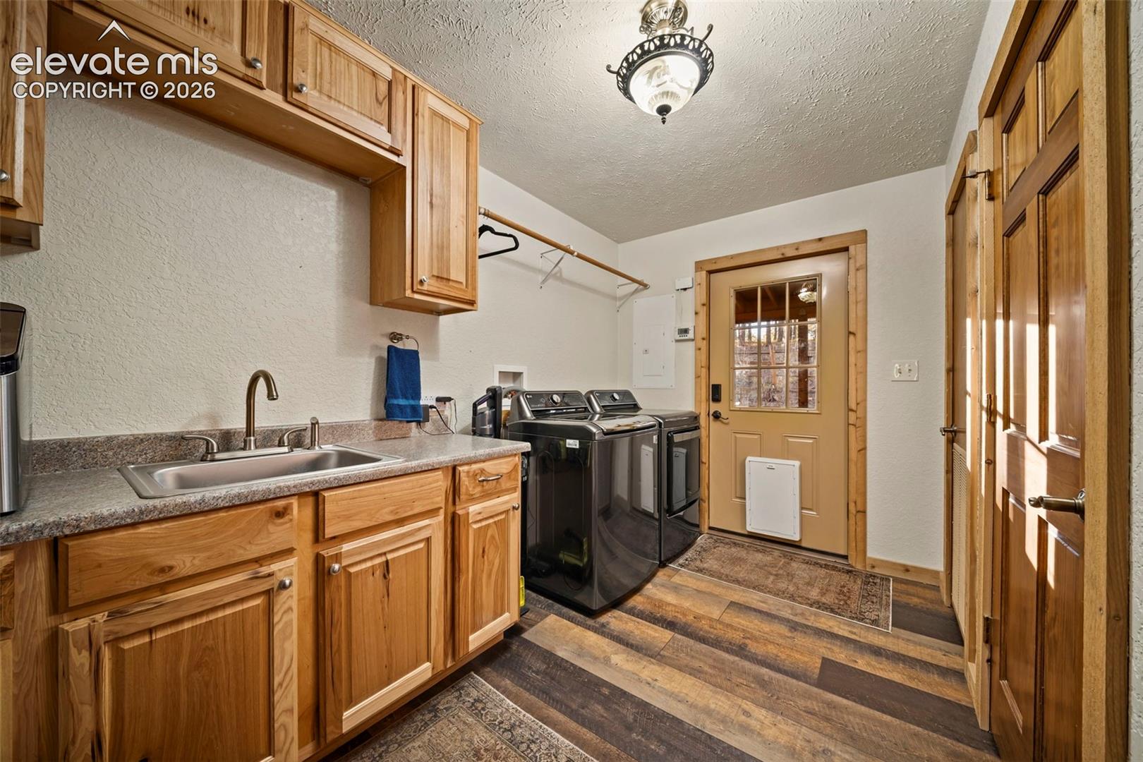 Laundry room featuring wood-finish cabinetry, stone-composite countertop with integrated stainless steel sink, wood-finish flooring, and solid wood interior doors