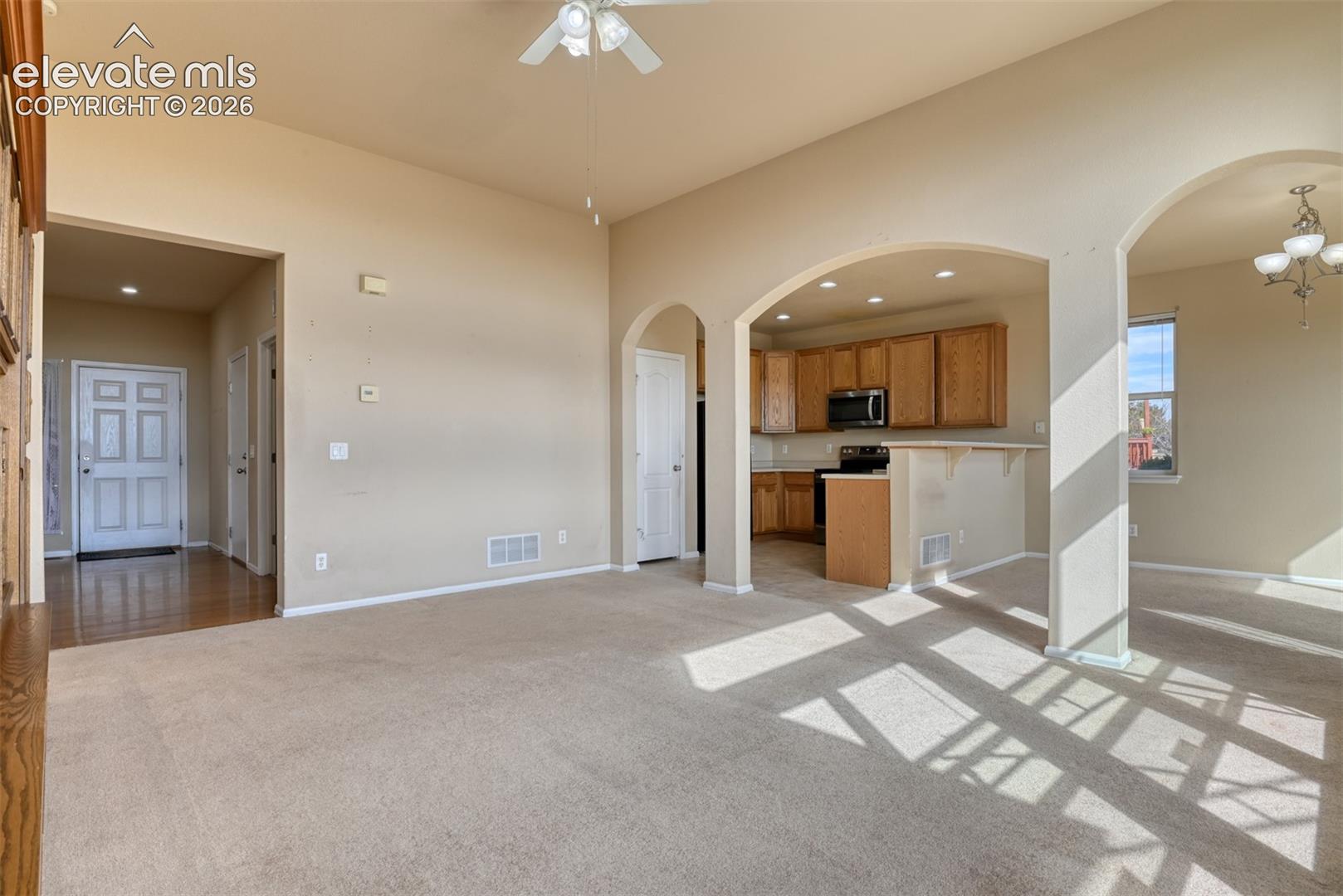 High ceilings featuring a central fan, architectural arched entryways, recessed lighting, and kitchen cabinetry with a wood finish