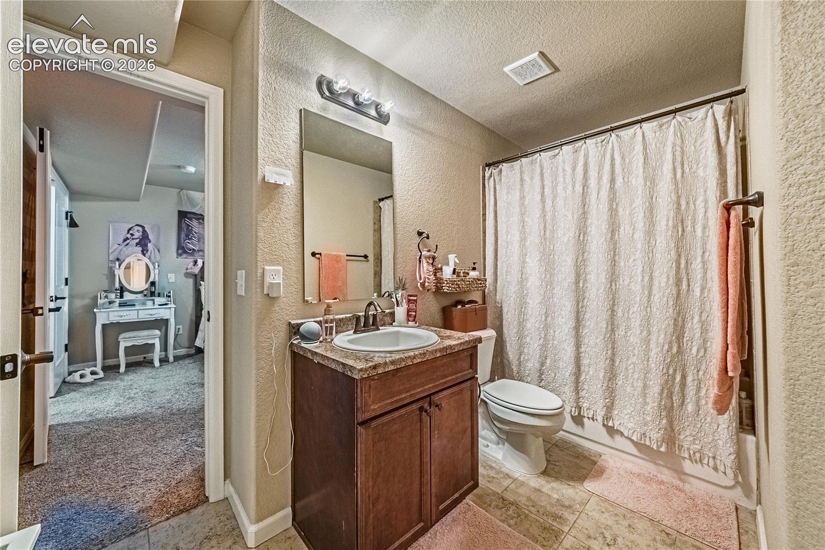Full bath with a textured wall, vanity, shower / tub combo, a textured ceiling, and light tile patterned floors