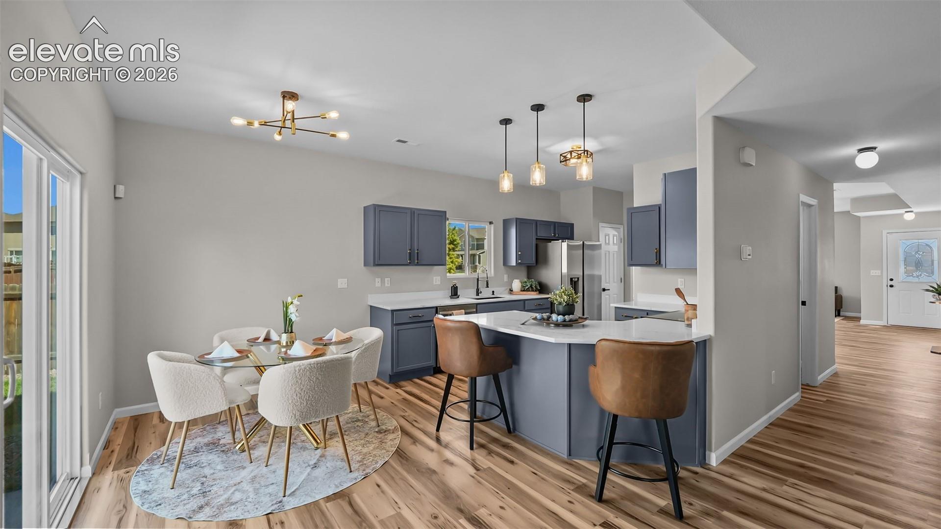 Kitchen and dining area featuring wood-finish flooring, a kitchen island with seating, pendant lighting fixtures, and sliding glass doors